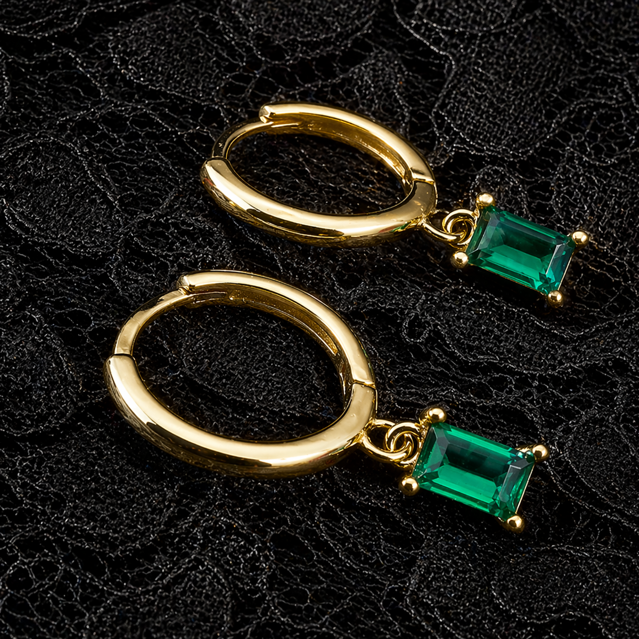 Gold hoop earrings with green gemstones on a black lace background
