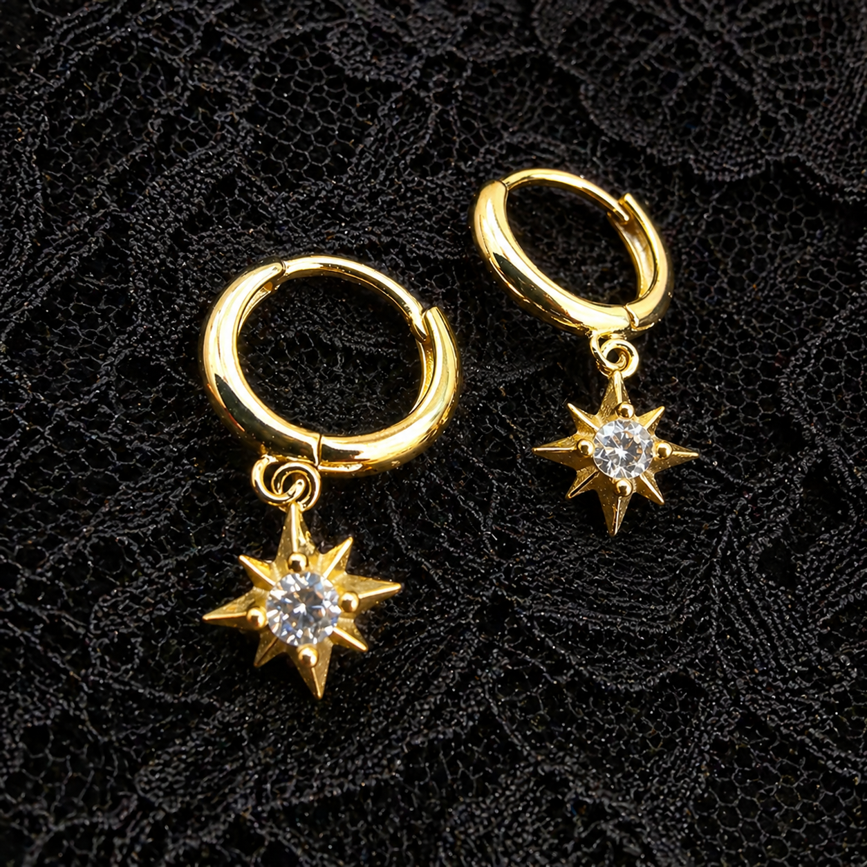 Gold hoop earrings with star-shaped charms on a black textured background