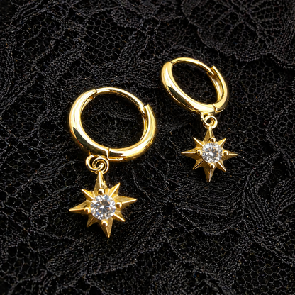 Gold hoop earrings with star-shaped charms on a black textured background