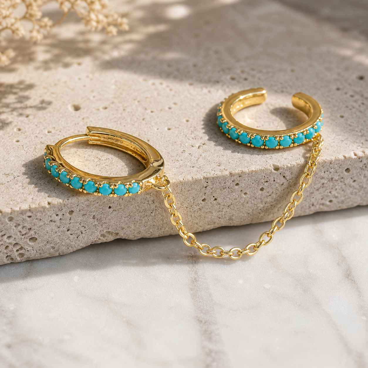 Gold hoop earrings with turquoise stones on a stone surface