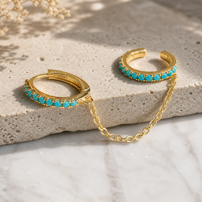 Gold hoop earrings with turquoise stones on a stone surface