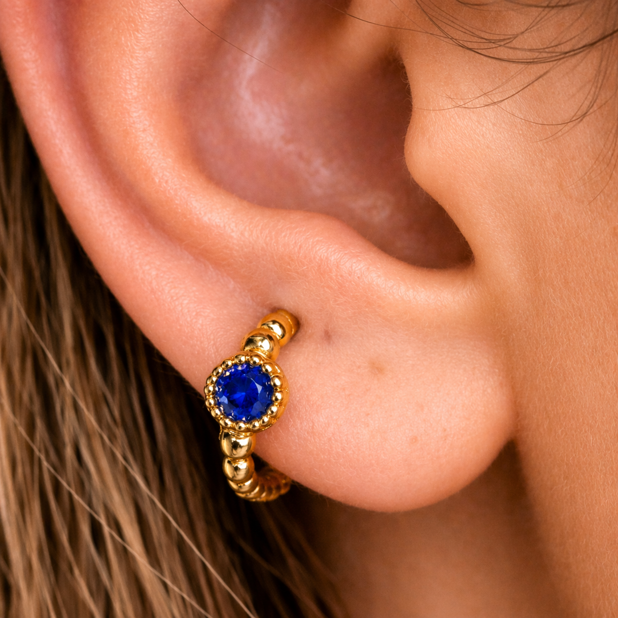 Close-up of an ear wearing a gold earring with a blue gemstone.