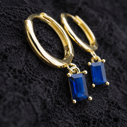 Gold hoop earrings with blue gemstones on a black textured background