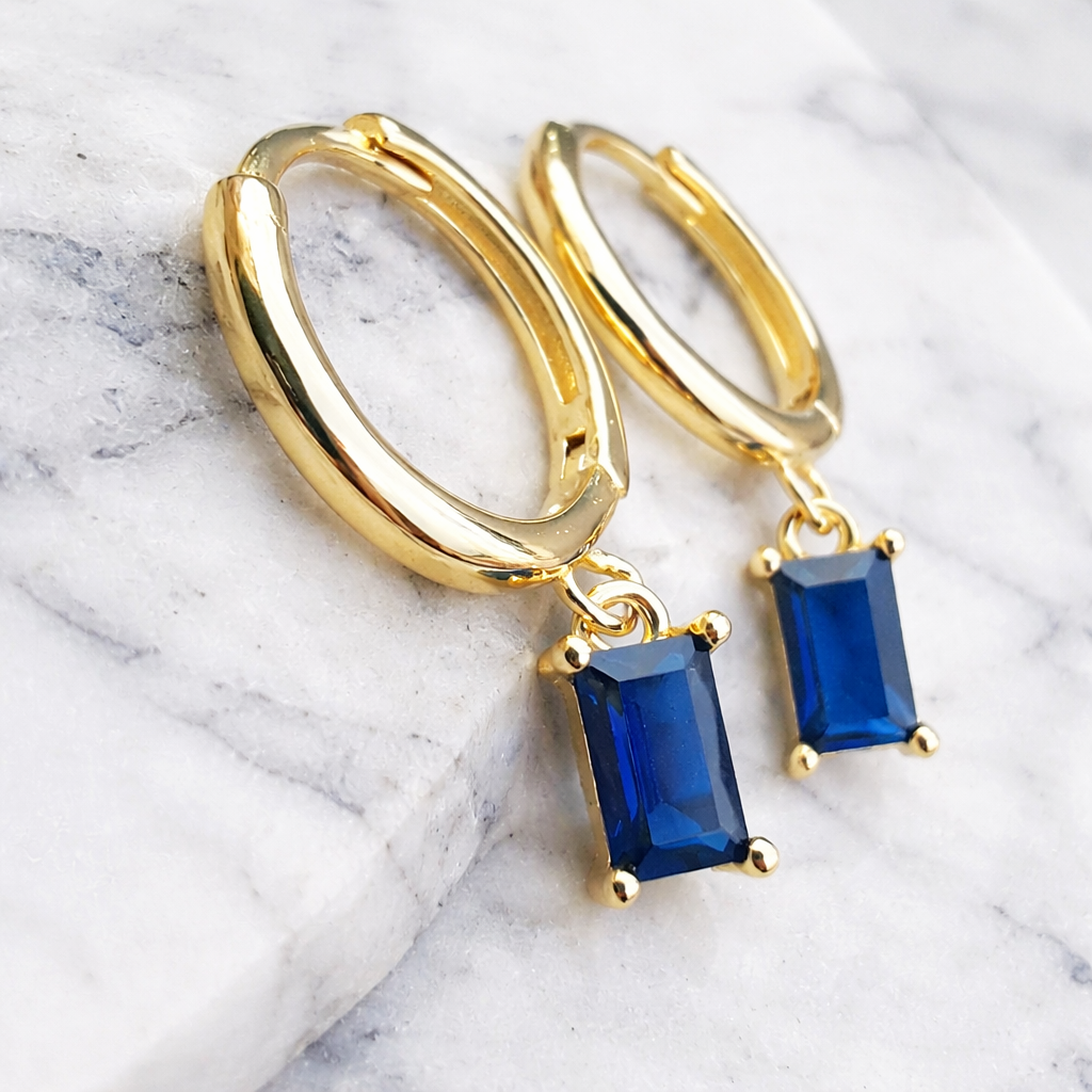 Gold hoop earrings with blue gemstones on a marble surface
