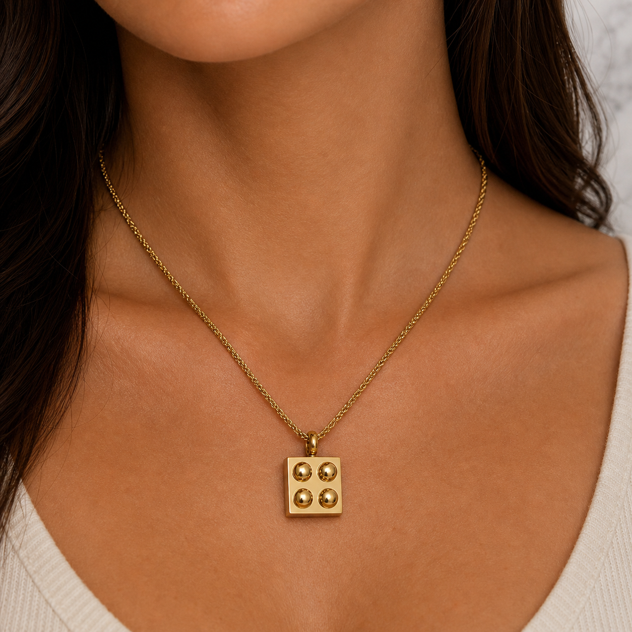 Gold necklace with a square pendant worn by a person
