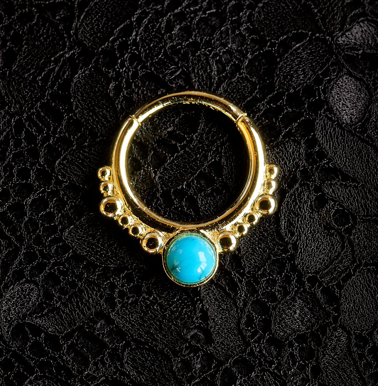 Gold nose ring with a turquoise stone on a black textured background