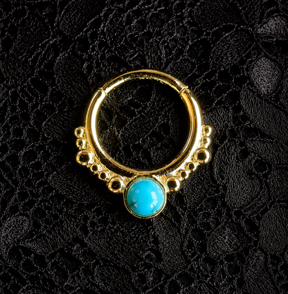 Gold nose ring with a turquoise stone on a black textured background