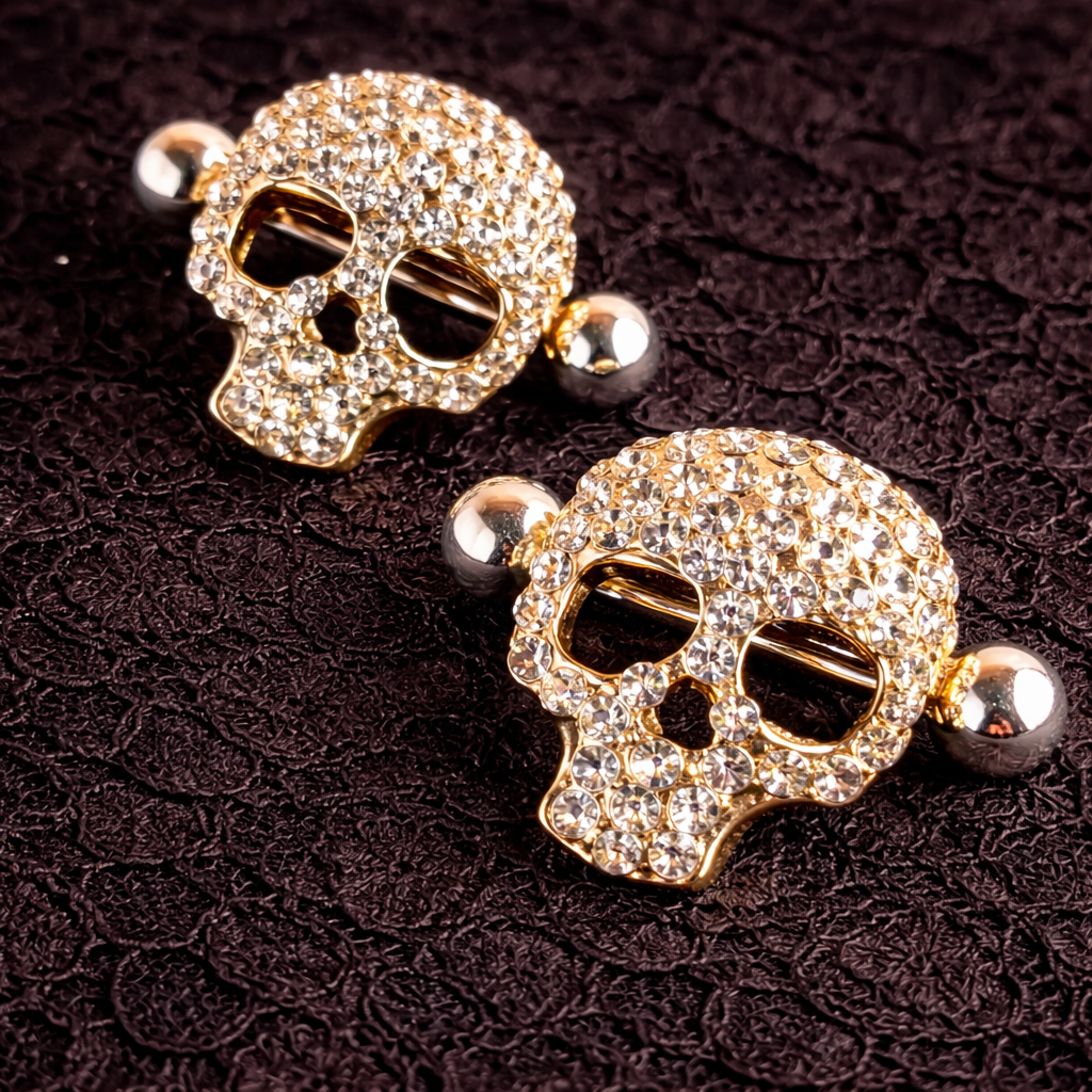 Gold skull-shaped nipple shields with gemstones on a dark textured background