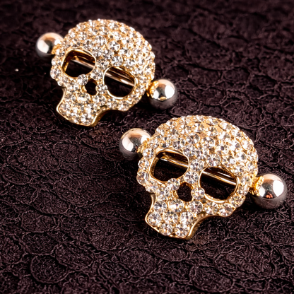 Gold skull-shaped nipple shields with gemstones on a dark textured background