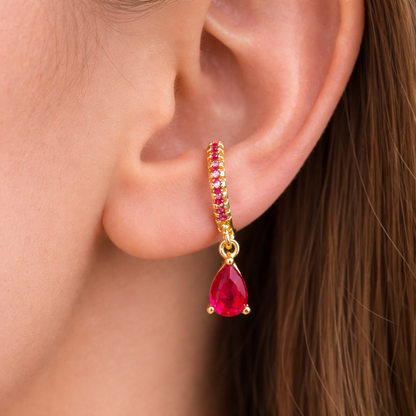 Close-up of an ear wearing a gold earring with red gemstones.