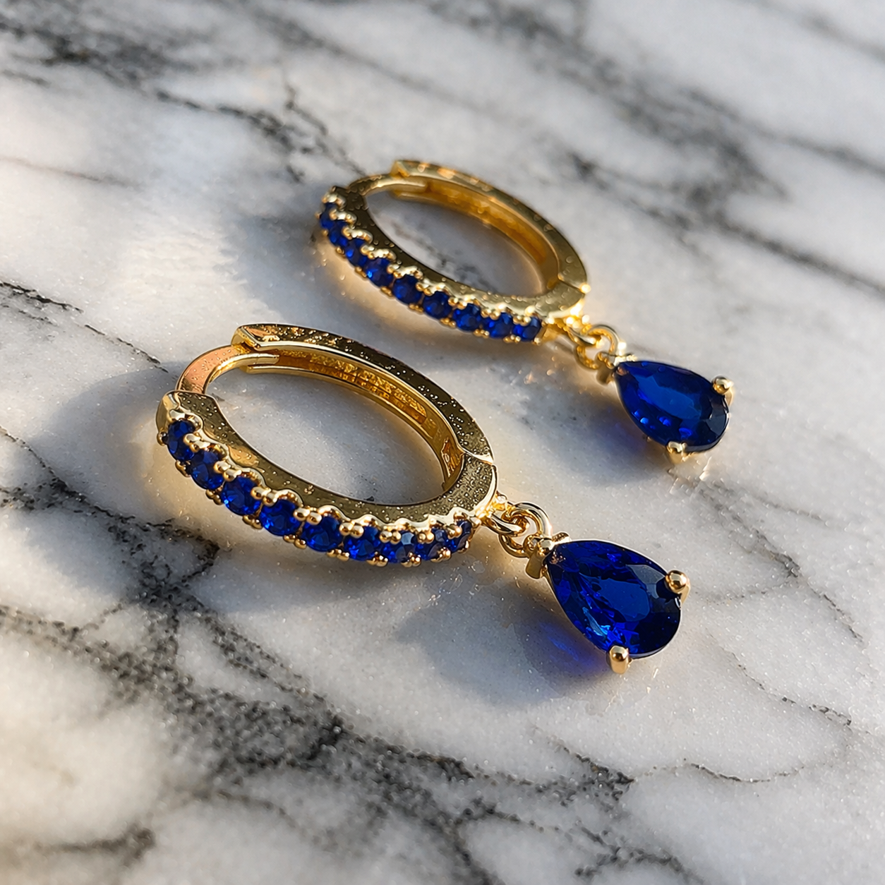 Gold hoop earrings with blue gemstones on a marble surface