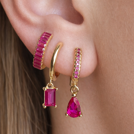 Gold hoop earrings with pink gemstones worn on an ear