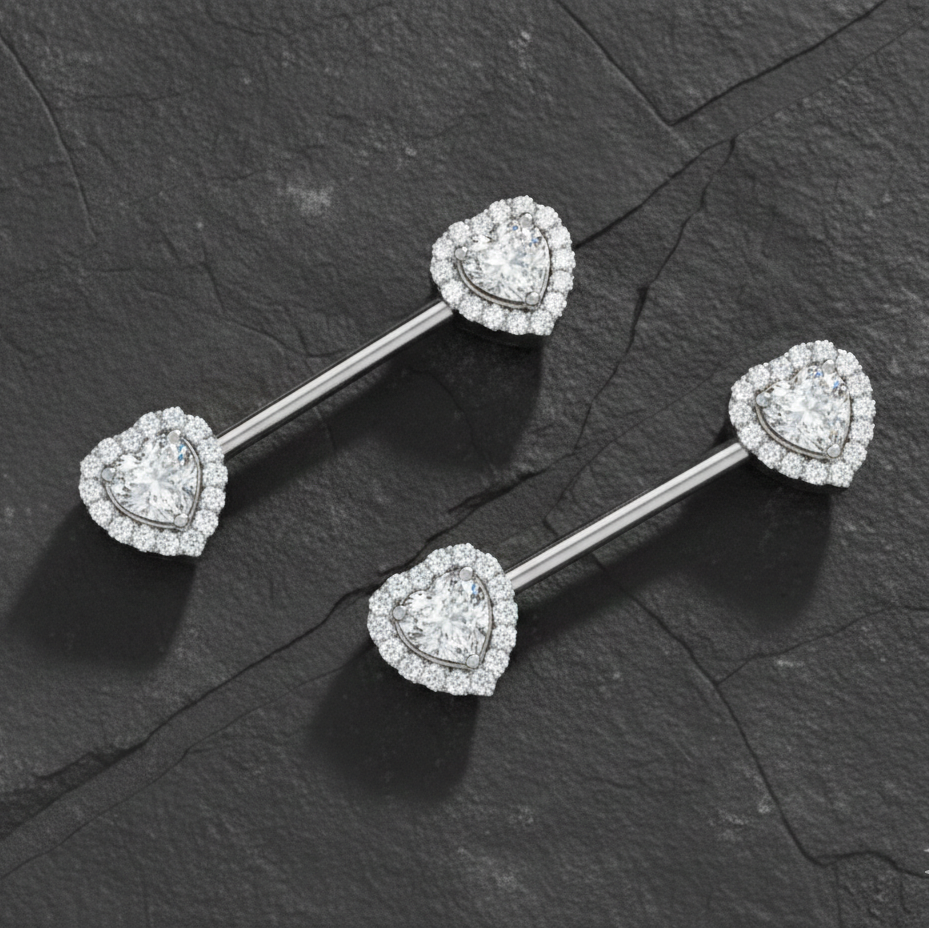 Heart-shaped diamond nipple piercing bars on a dark stone surface