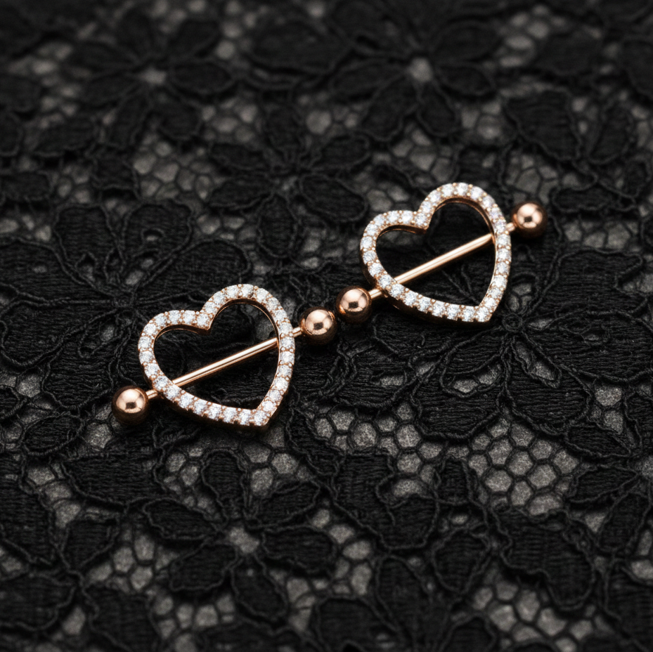 Heart-shaped nipple piercing shields on a black lace background