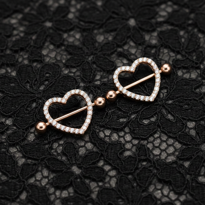 Heart-shaped nipple piercing shields on a black lace background
