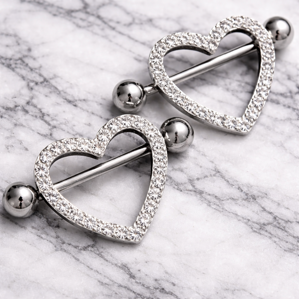 Heart-shaped silver nipple shields with gemstones on a marble surface
