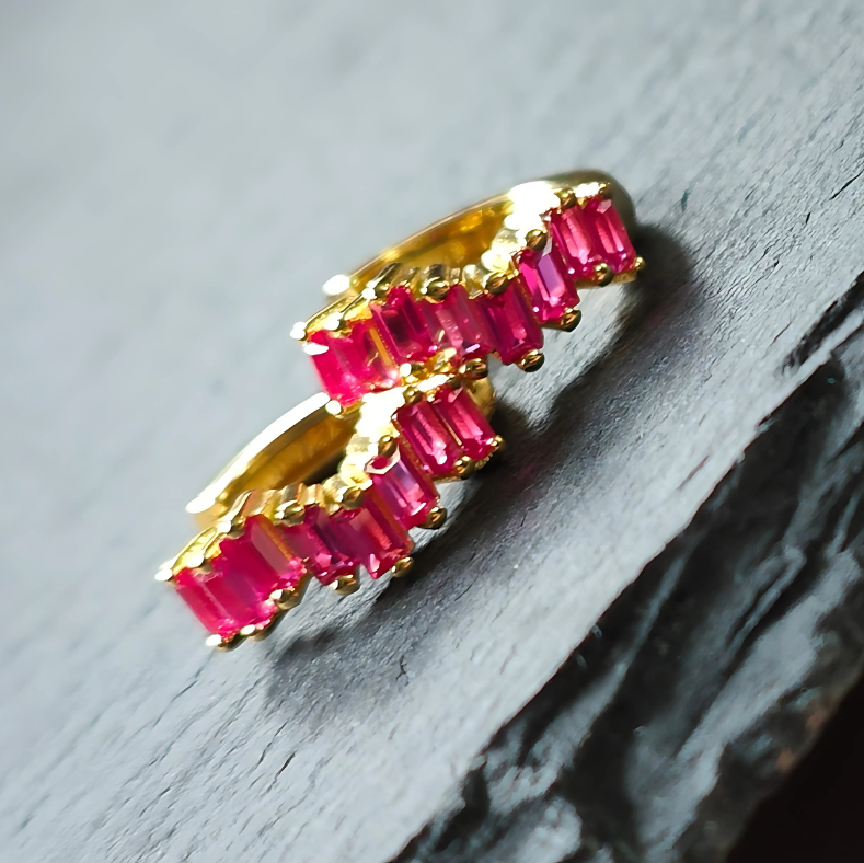 Close-up of 18K gold-plated huggie earrings with vivid magenta cubic zirconia stones set in 925 sterling silver, showcasing intense color and shine.