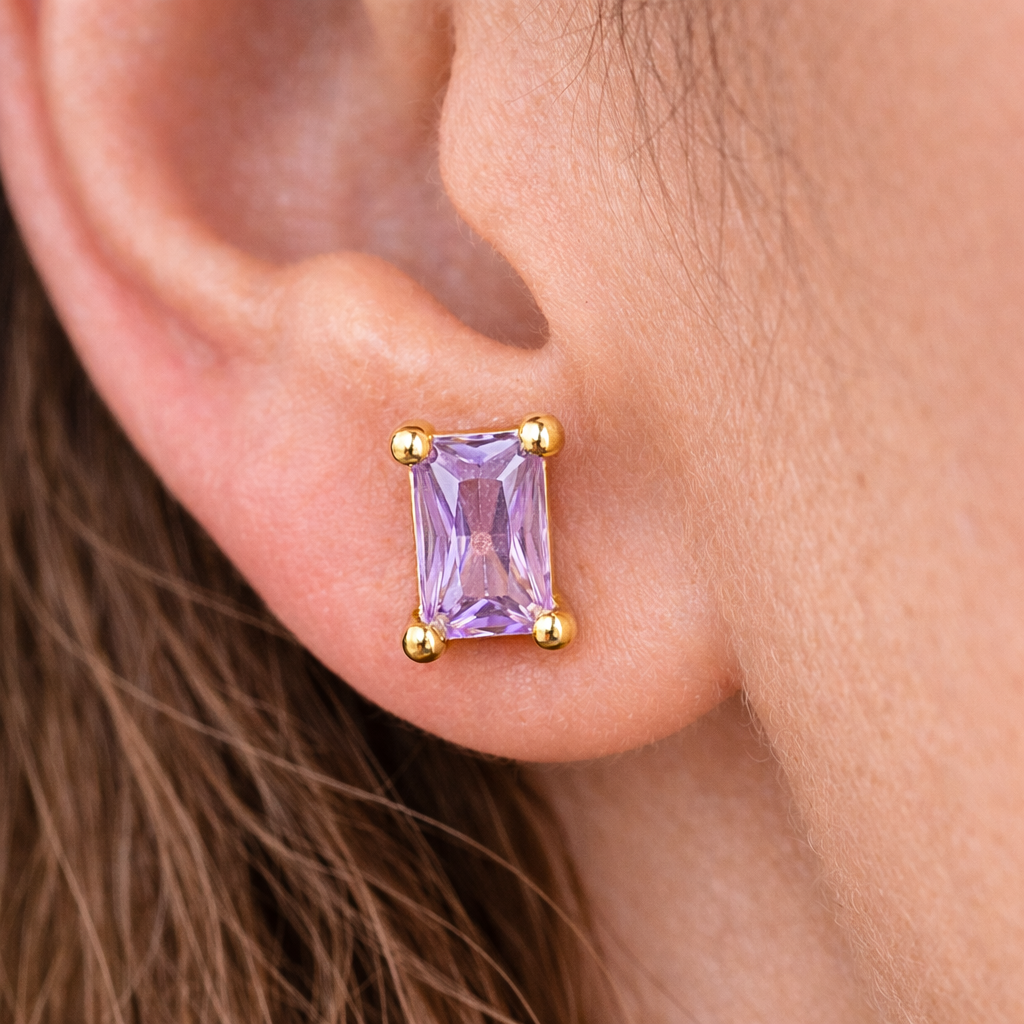 Gold earring with a purple gemstone worn by a person.
