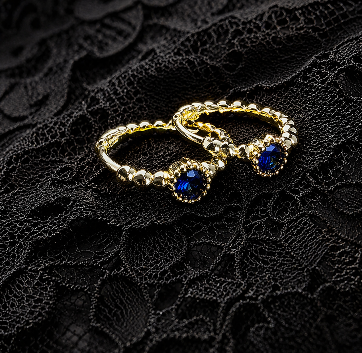 Pair of gold hoop earrings with blue gemstones on a black lace background