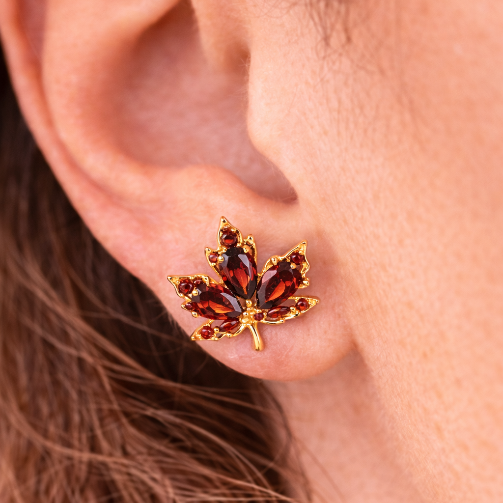 Close-up of an ear wearing a gold and red gemstone leaf earring.