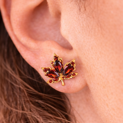 Close-up of an ear wearing a gold and red gemstone leaf earring.