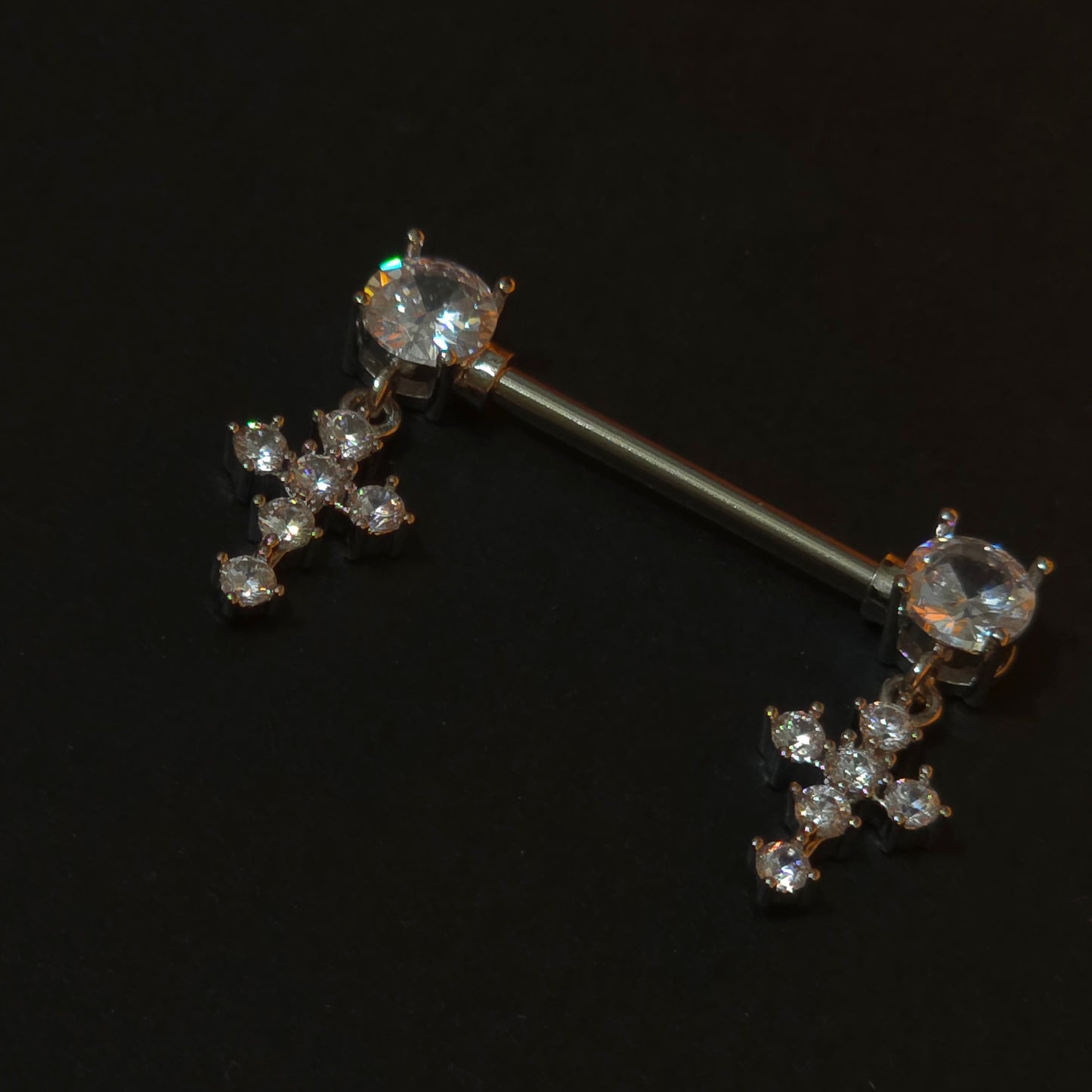 Nipple piercing bars with cross gemstones on a black background