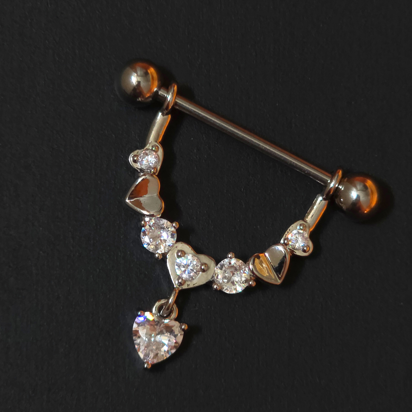 Nipple piercing ring with heart and diamond designs on a black background