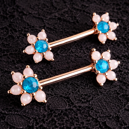 Pair of floral nipple bars with blue gemstones and pearl-like centers on a dark background