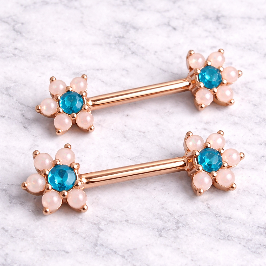 Pair of rose gold barbell nipple bars with blue gemstones and pink stones on a marble background
