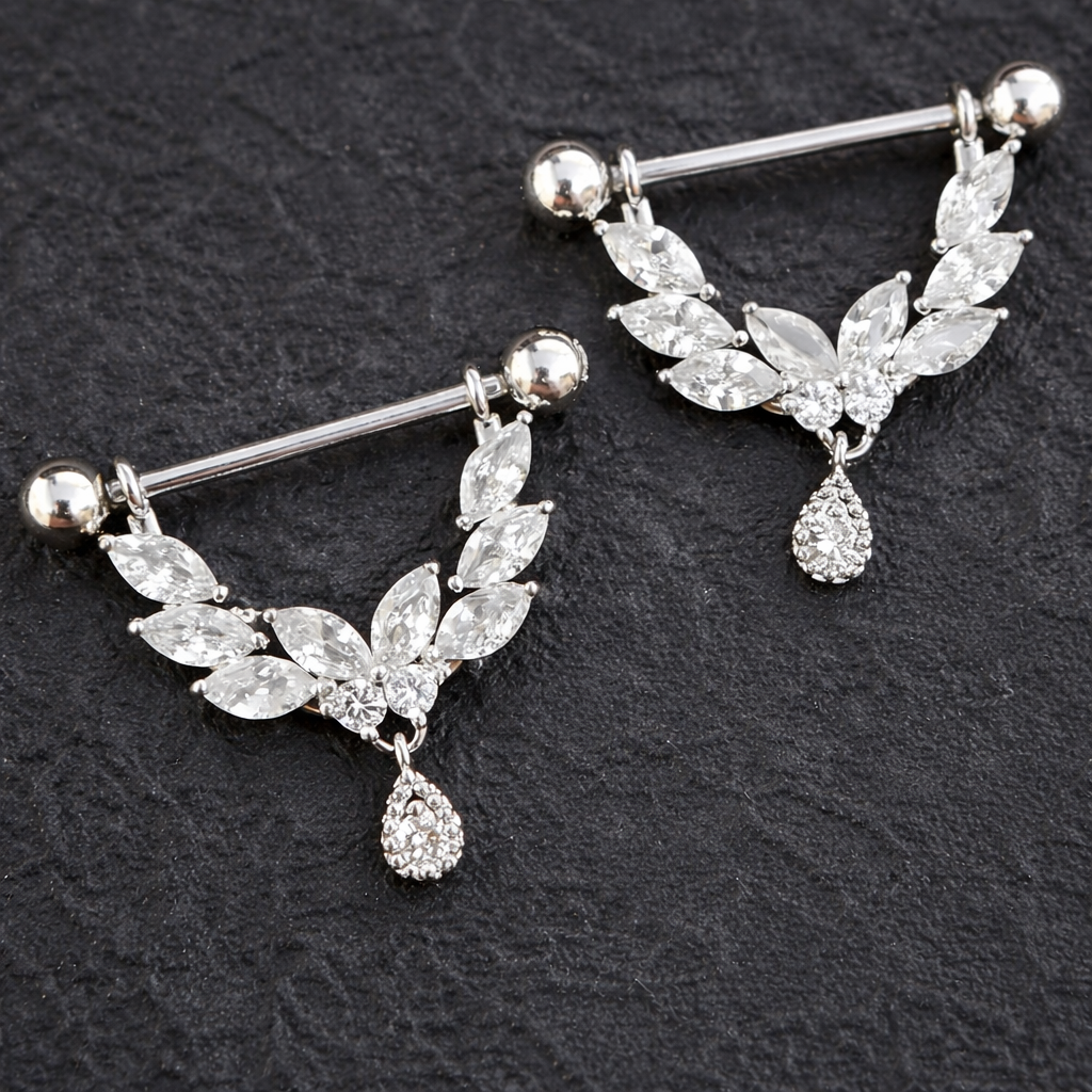 Pair of silver dangle nipple shields with leaf and teardrop designs on a dark background