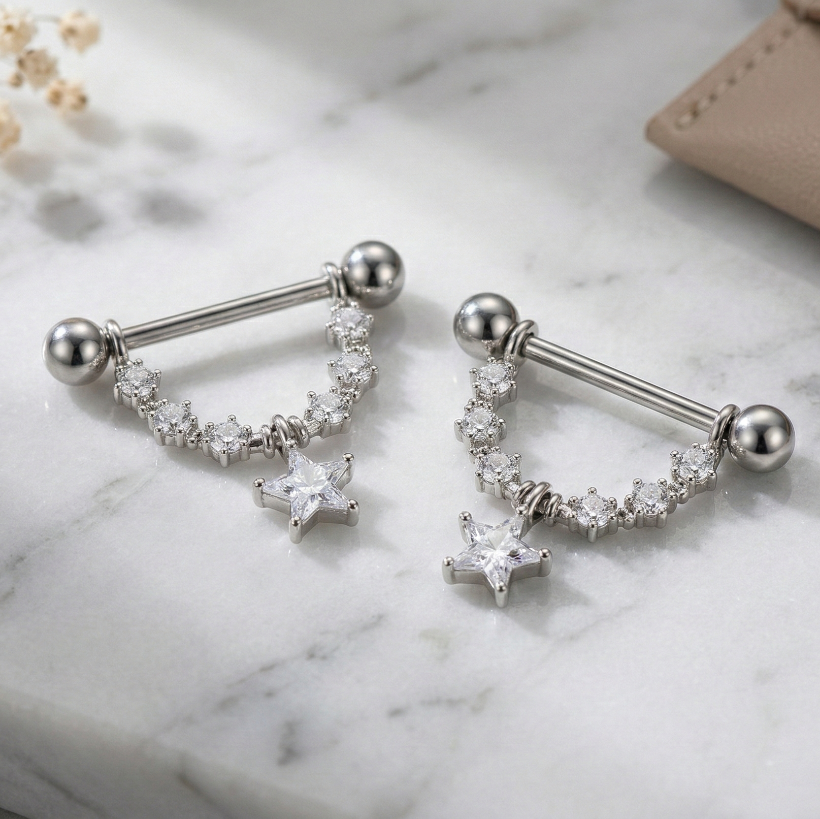Pair of silver dangle nipple shields with star designs on a marble surface.