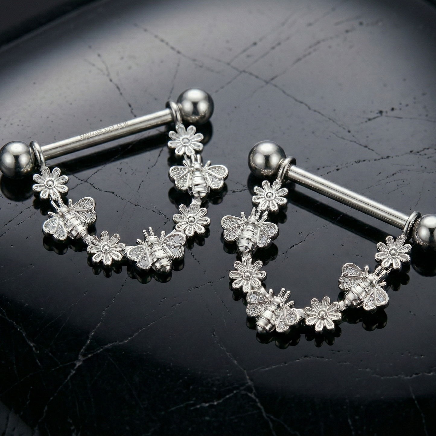 Pair of silver floral nipple shields with bees on a black background