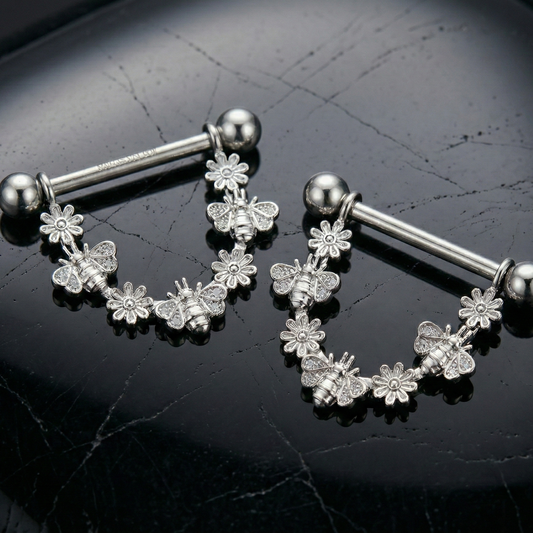 Pair of silver floral nipple shields with bees on a black background