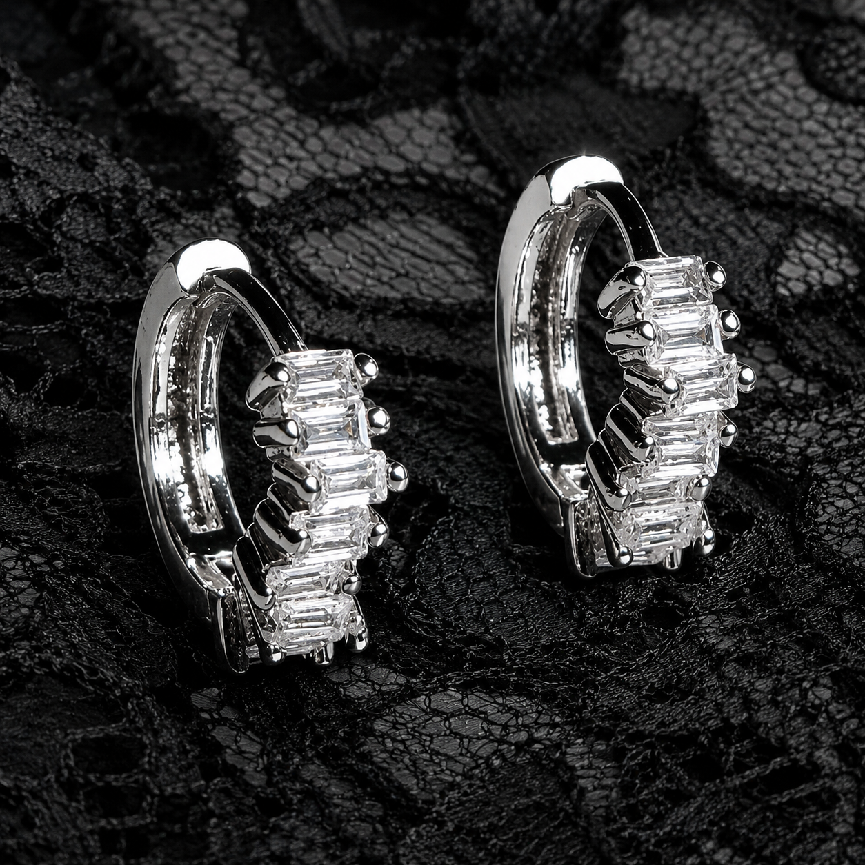 Pair of silver hoop earrings with clear gemstones on a textured black background
