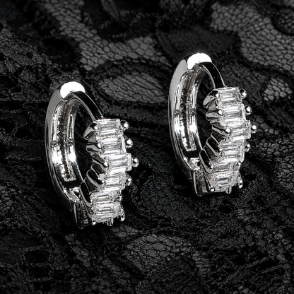 Pair of silver hoop earrings with clear gemstones on a textured black background