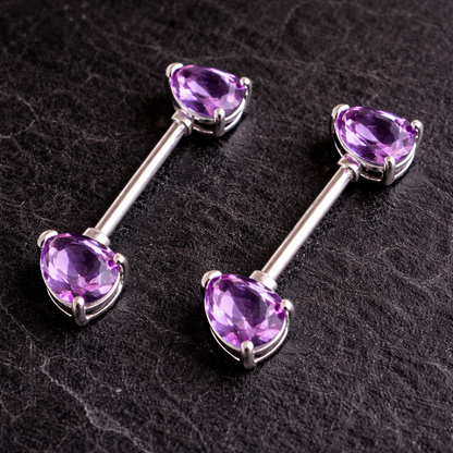 Pair of silver nipple bars with purple gemstones on a dark textured background