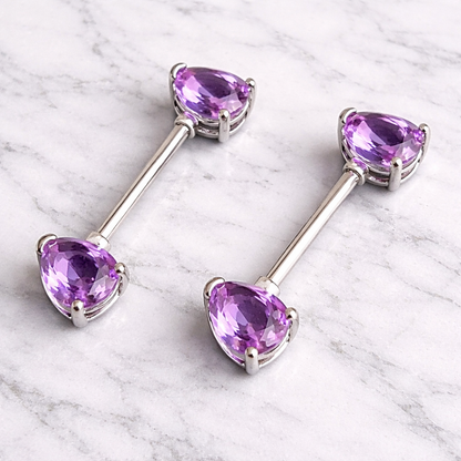 Pair of silver nipple bars with purple gemstones on a marble surface
