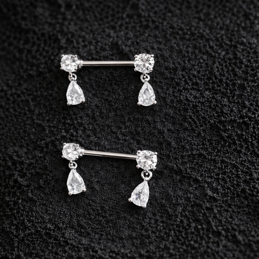 Pair of silver nipple bars with teardrop-shaped gemstones on a textured black background.