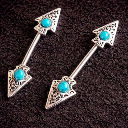 Pair of silver nipple bars with turquoise gemstones on a dark textured background