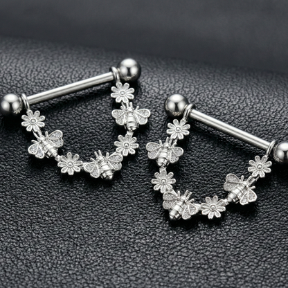 Pair of silver nipple piercing bars with floral designs on a black textured background