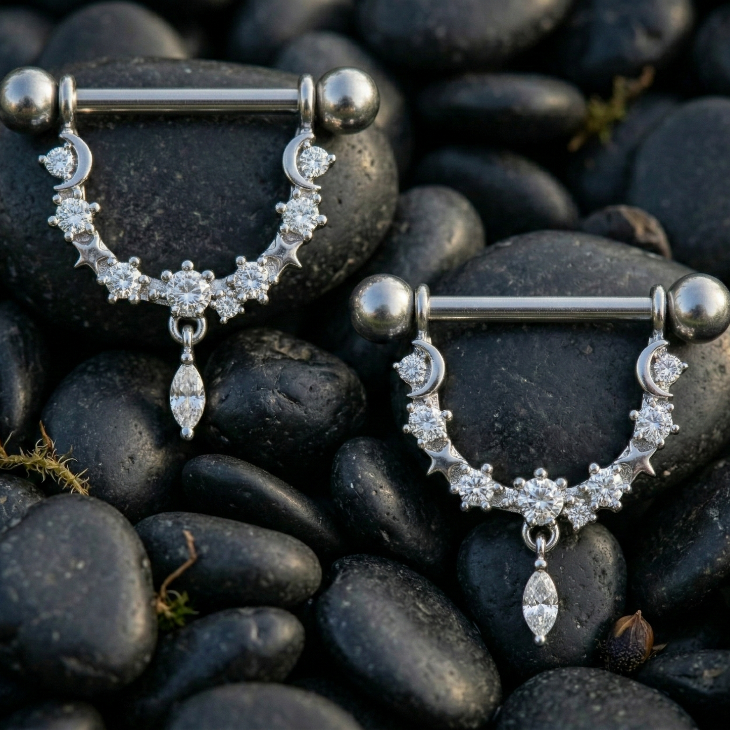 Pair of silver nipple piercing bars with gemstones on dark pebbles