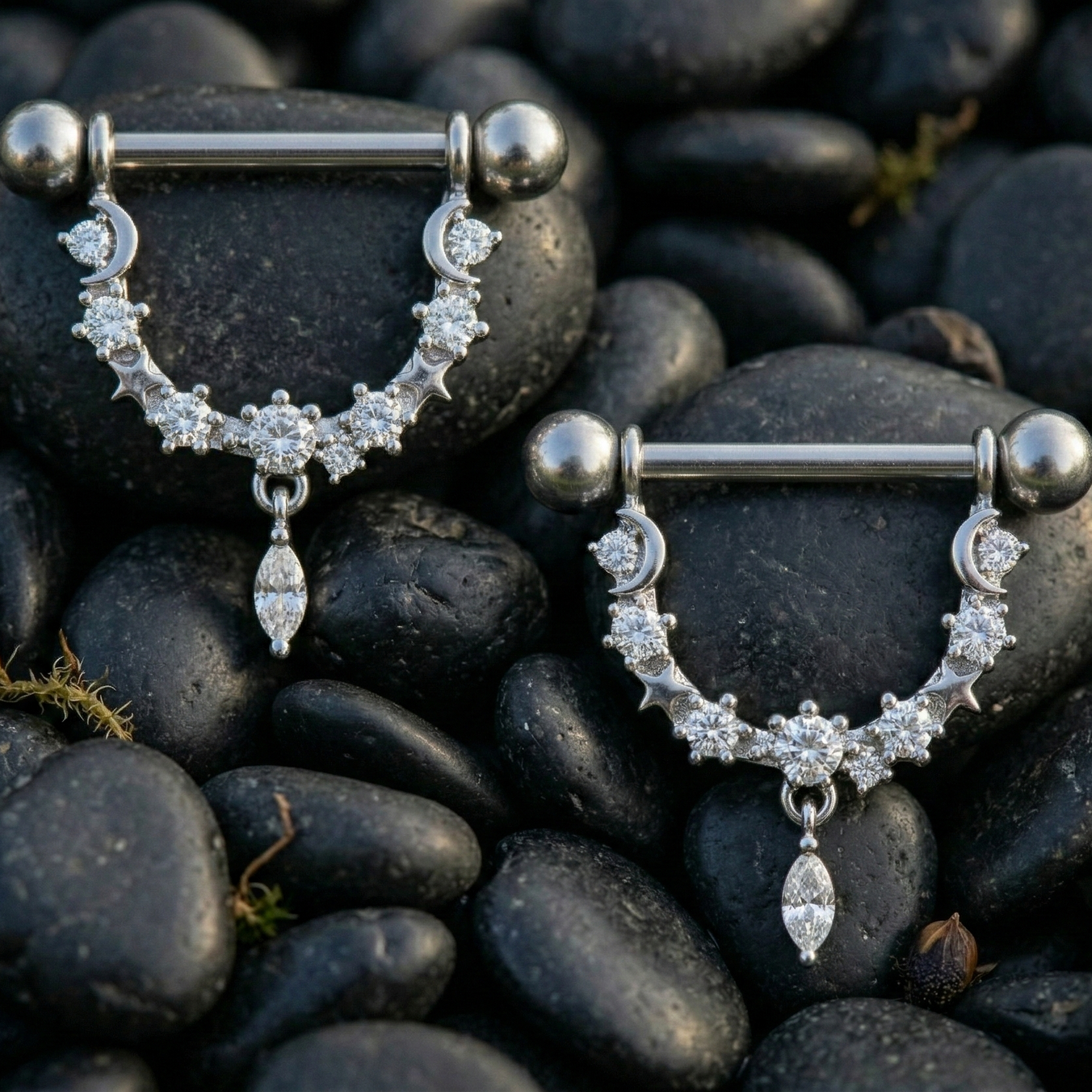 Pair of silver nipple piercing bars with gemstones on dark pebbles