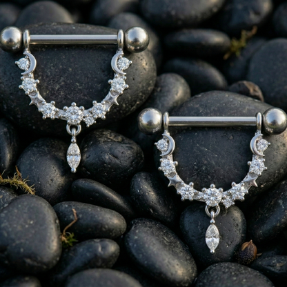 Pair of silver nipple piercing bars with gemstones on dark pebbles