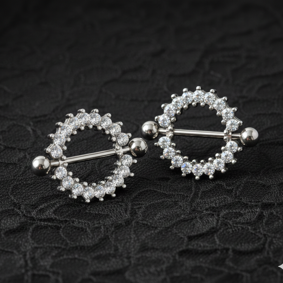 Pair of silver nipple rings with circular designs on a textured black background