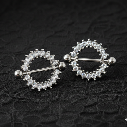 Pair of silver nipple rings with circular designs on a textured black background