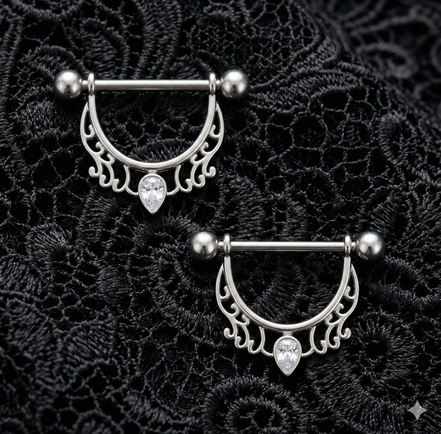 Pair of silver nipple shields rings with decorative designs on a black lace background