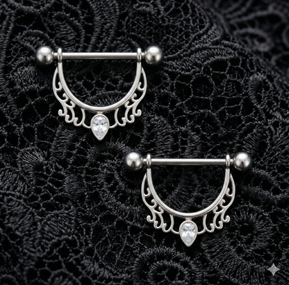 Pair of silver nipple shields rings with decorative designs on a black lace background