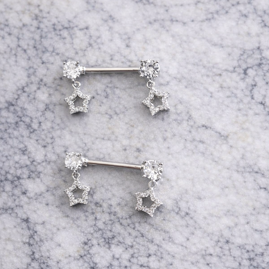 Pair of silver star-shaped nipple piercing bars on a marble surface