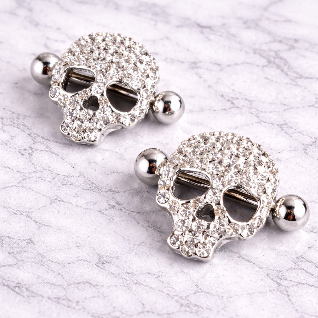 Pair of skull-shaped nipple bars with rhinestones on a marble surface