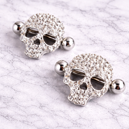 Pair of skull-shaped nipple bars with rhinestones on a marble surface